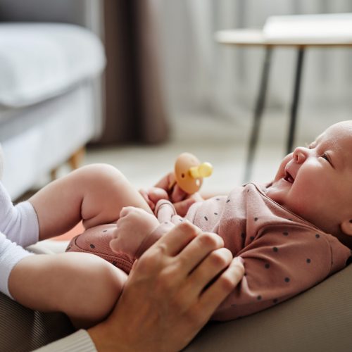 Side view of mother playing with laughing baby girl lying on her knees spending time at home