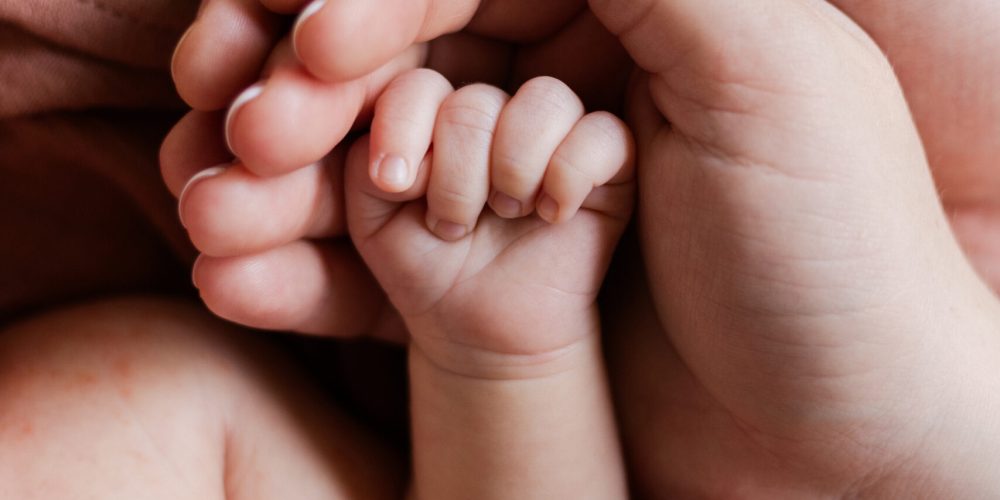 A heartwarming close-up of a newborn baby’s tiny hand cradled in the loving hands of parents